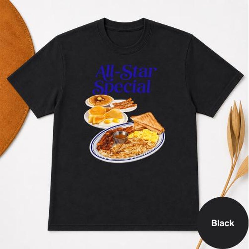 May include: Black t-shirt with a blue graphic that reads "All-Star Special." The graphic features a plate of breakfast food, including eggs, bacon, toast, and pancakes. A black circle with the word "Black" is in the bottom right corner.