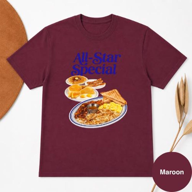 May include: Maroon t-shirt with the text "All-Star Special" in blue. The graphic features a plate of breakfast food, including pancakes, eggs, bacon, toast, and hash browns. A color swatch at the bottom right reads "Maroon".