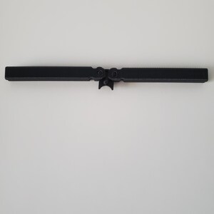 May include: A black, hinged metal object, possibly a tool or hardware component, is centered against a white background. The object has a rectangular shape with a central hinge and circular features on either side.