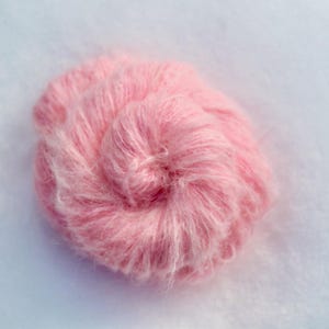 Puede incluir: Un ovillo de hilo suave y rosa, perfecto para tejer o hacer ganchillo.