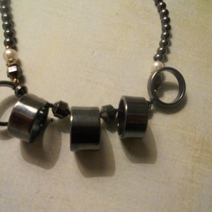 May include: A black necklace with silver and gold accents. The necklace has several round metal charms hanging from it.