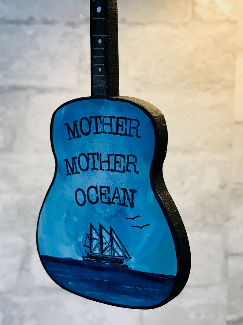 May include: A blue wooden guitar with the words "Mother Ocean" painted on the body. A small sailboat is painted on the body of the guitar.