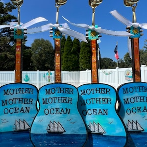 May include: Four blue and white painted wooden guitar ornaments with the text "Mother Mother Ocean" on each. The ornaments are hanging from gold clips with white ribbon.