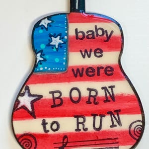 May include: A red, white, and blue guitar-shaped ornament with the text "baby we were born to run".