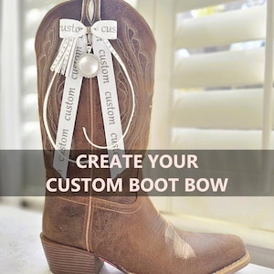 May include: A brown leather western boot adorned with a white ribbon bow featuring the repeating text custom and a central circular charm with a silver border. The text CREATE YOUR CUSTOM BOOT BOW is overlaid across the center of the image.