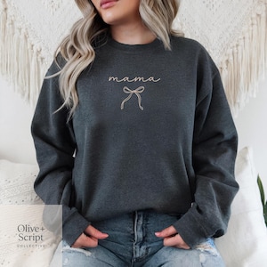 May include: Dark gray sweatshirt with the word "mama" in cursive script and a bow graphic. The sweatshirt is a solid color and has long sleeves. The Olive + Script Collective logo is in the bottom left corner.