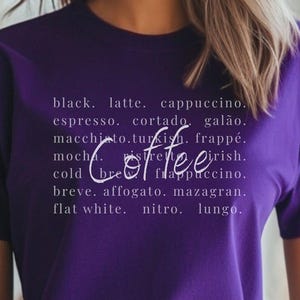 May include: A purple t-shirt featuring the word "Coffee" in a cursive font, with a list of coffee types in white text. The person is wearing blue jeans.