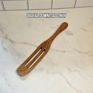 Puede incluir: Una espátula de cocina de madera marrón con un mango largo y dos ranuras verticales en la cabeza plana. El texto DIGITAL DOWNLOAD ONLY está impreso en negro sobre la espátula. La veta de la madera es visible en todo el utensilio.