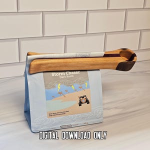 May include: A wooden coffee bag clip with a dark wood accent on the handle, clamped onto a light blue coffee bag labeled Storm Chaser Dark Roast with an illustration of palm trees, lightning, and a vehicle. The text DIGITAL DOWNLOAD ONLY is visible.