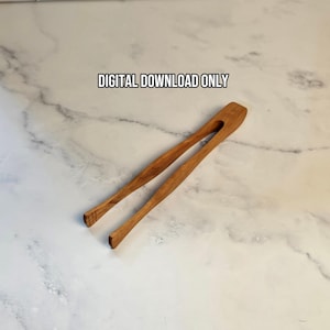 May include: A pair of wooden kitchen tongs with a natural brown grain finish. The text DIGITAL DOWNLOAD ONLY is printed in black above the tongs. The tongs feature a single-piece construction with a flexible bridge connecting the two arms.