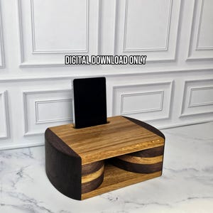 Peut inclure: Un support de téléphone rectangulaire en bois présentant des motifs de grain de bois alternant chêne clair et noyer foncé avec une fente centrale pour smartphone. Le texte DIGITAL DOWNLOAD ONLY est visible au-dessus du support aux côtés incurvés.