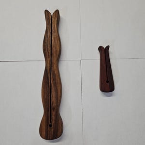 Puede incluir: Dos herramientas de madera para madejas. El swift más grande es de color marrón oscuro con un diseño delgado y curvo y una parte superior dividida. El swift más pequeño tiene un diseño similar. Ambos tienen un agujero en la base.