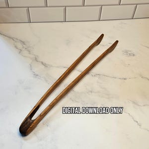 Pode incluir: Um par de pinças de cozinha de madeira longas e finas com um padrão de grão de madeira castanho escuro e um design de cabo curvo. O texto "DIGITAL DOWNLOAD ONLY" está impresso em letras pretas na superfície perto do centro das pinças.