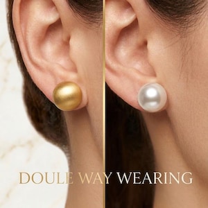 Peut inclure: Une paire de boucles d'oreilles à tige au design sphérique. L'une présente une finition dorée mate, tandis que l'autre possède une surface blanche lisse et lustrée rappelant une perle. Le texte "DOULE WAY WEARING" est inscrit en bas.