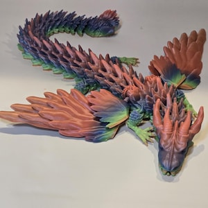 May include: A colorful, articulated dragon figurine. The dragon features a detailed design with a mix of pink, blue, green, and orange hues. The wings and body are intricately textured, showcasing a fantasy creature.