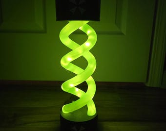 May include: A unique, glowing green lamp with a spiral design, featuring embedded lights. The lamp has a black base and a black lampshade with a symbol. The overall design is reminiscent of a DNA helix.