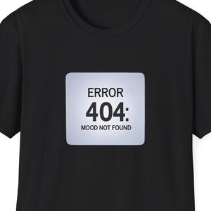 Op de afbeelding: Zwart t-shirt met een vierkante afbeelding op de voorkant. De afbeelding toont de tekst "ERROR 404: MOOD NOT FOUND" in witte letters op een lichtgrijze achtergrond. Het t-shirt heeft korte mouwen en een ronde hals.