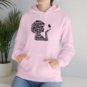 May include: A light pink hoodie with a front pocket and a drawstring hood. The black graphic on the front depicts a woman's silhouette with words like "Strong", "Beautiful", and "Independent" forming her hair and a butterfly.