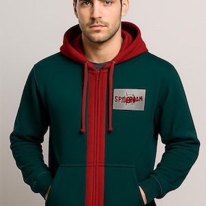 May include: A green zip-up hoodie with a red hood and a red stripe down the center. The hoodie features a Spider-Man logo patch on the chest. The model is wearing a gray t-shirt underneath.