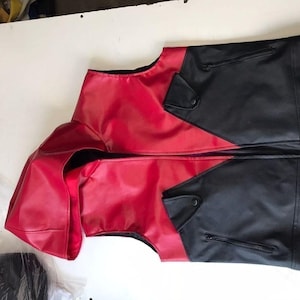 May include: A two-tone vest in red and black. The vest features a red front and hood, with black panels on the sides and back. It has a zipper closure and small pockets. The garment is made of a smooth, possibly leather-like material.