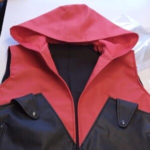 May include: A red and black hooded vest with two front pockets. The vest features a red hood and upper section, with a black lower section and pockets. The vest is made of a smooth material and has a zipper.