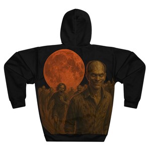 May include: Black hooded sweatshirt featuring a zombie-themed graphic. The design includes a large orange moon, a crowd of zombies, and a close-up of a smiling zombie. The artwork is detailed and has a horror theme.