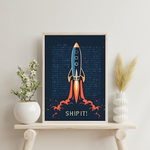 May include: A framed art print showing a blue and orange rocket ship taking off against a dark blue backdrop with binary code. The words "SHIP IT!" are in white at the bottom. The rocket has three circular windows. The print is in a wooden frame.