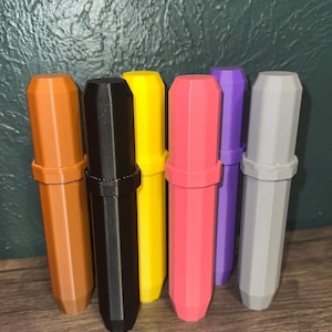 May include: A collection of seven colorful, cylindrical containers. The containers are in shades of brown, black, yellow, pink, purple, and gray. Each container has a cap and a body with a geometric design.
