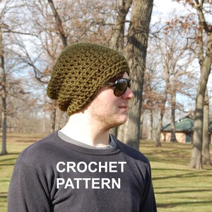 May include: A green crocheted beanie with a slouchy fit. The beanie is worn by a person wearing sunglasses and a black long-sleeved shirt. The text "CROCHET PATTERN" is printed on the shirt.