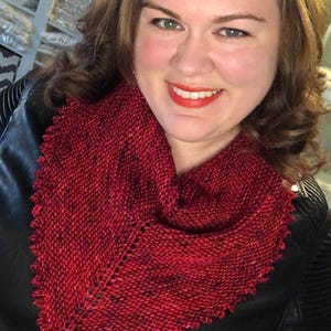 May include: A red knitted scarf with a scalloped edge. The scarf is worn by a person with brown hair and is made of a soft, textured yarn.