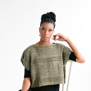 May include: A woman wearing a green crochet top with a black skirt, sitting on a white chair.