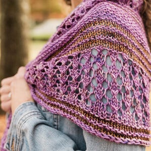 May include: A hand-knitted shawl featuring a variegated purple yarn with sections of brown and tan. The design incorporates a textured openwork lattice stitch pattern alternating with solid garter stitch bands, draped over a light blue denim jacket.