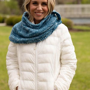 Könnte beinhalten: Eine Frau trägt eine weiße Steppjacke mit einem blauen gestrickten Infinity-Schal. Der Schal ist hellblau mit einem gesprenkelten Muster.