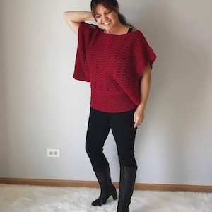 May include: A woman wearing a red crocheted top with black trousers and black knee-high boots.