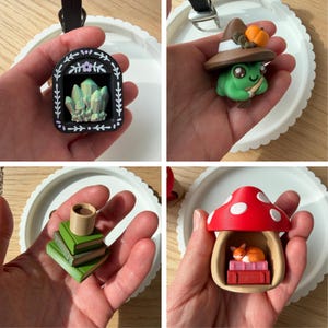 May include: A collection of four miniature charms featuring a black arched frame with crystals, a green frog wearing a brown witch hat with a pumpkin, a stack of three green books with a cup, and a red mushroom house containing a sleeping fox.