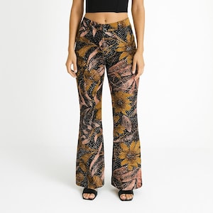 Puede incluir: Un top bustier negro con tirantes finos combinado con pantalones acampanados de cintura alta. Los pantalones presentan un estampado floral en tonos dorados, rosas y negros. El conjunto se presenta sobre un fondo blanco.