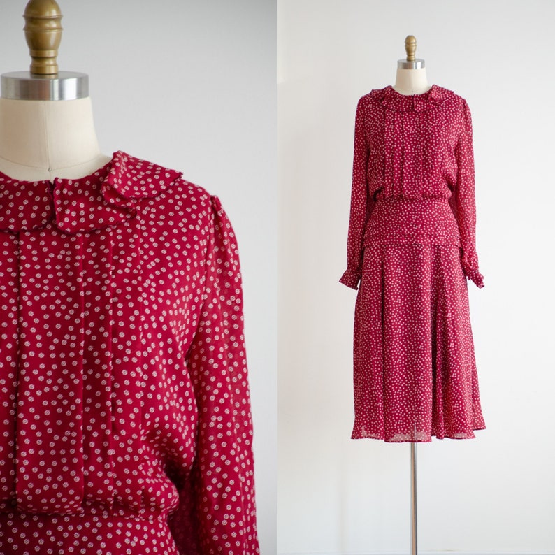 May include: A red dress with a white floral print and a peter pan collar. The dress has long sleeves and a gathered skirt.