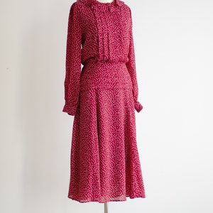 May include: A red dress with a white floral pattern. The dress has a ruffled collar and long sleeves. It is made of a lightweight fabric and has a flowing skirt.