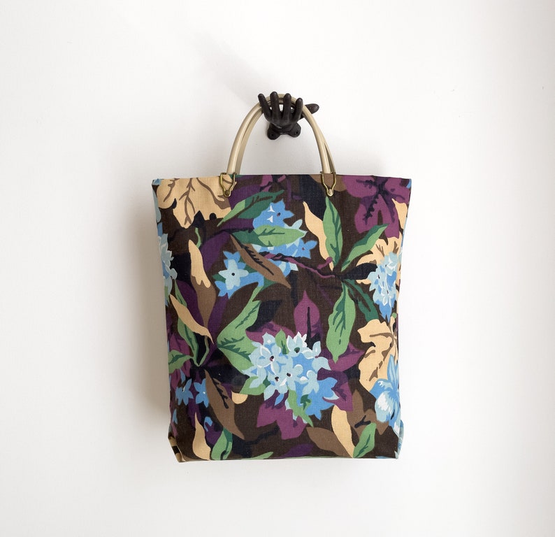 May include: A floral tote bag with a brown, green, purple, and blue floral pattern. The bag has two brown leather handles.
