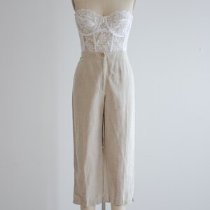 Puede incluir: Un top de cors&eacute; de encaje blanco combinado con pantalones de lino beige de cintura alta.