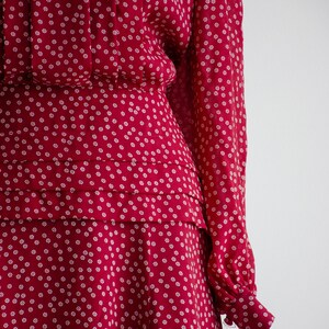 May include: A red dress with a white floral pattern. The dress has a fitted bodice and a full skirt. The sleeves are long and have a gathered cuff.