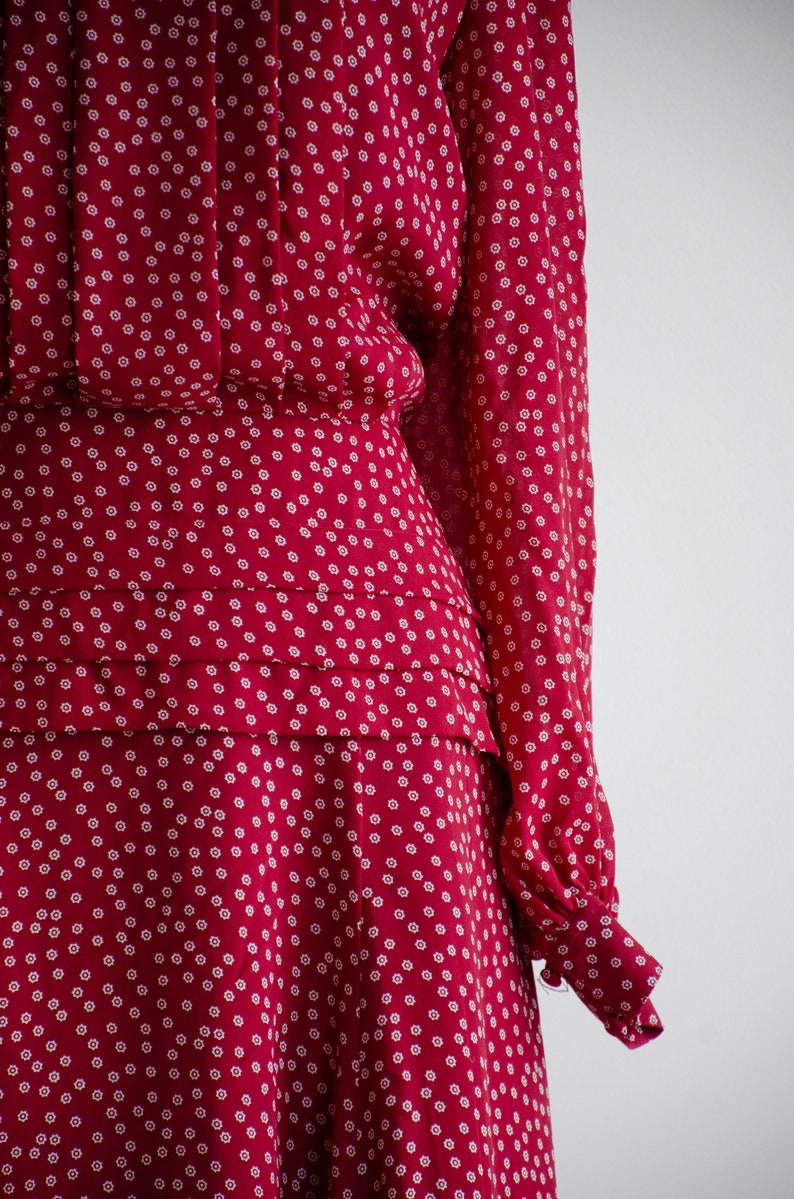 May include: A red dress with a white floral pattern. The dress has a fitted bodice and a full skirt. The sleeves are long and have a gathered cuff.