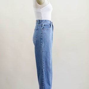May include: A side view of a white tank top and light blue denim jeans on a mannequin. The jeans have a high waist and a relaxed fit, with the cuffs rolled up. The tank top is a simple, fitted style.