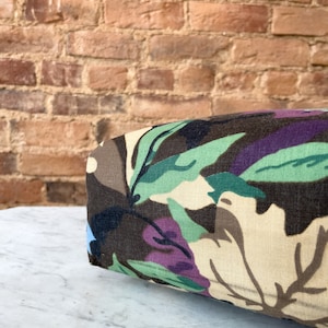 May include: A close-up of a brown, beige, green, and purple floral patterned fabric cushion. The cushion is sitting on a white marble surface.
