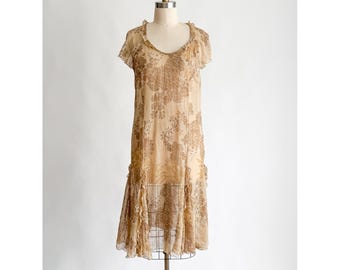 May include: A vintage-style beige dress with a floral pattern and ruffled hem. The dress features short sleeves and a scoop neckline. The dress is displayed on a mannequin against a white background.