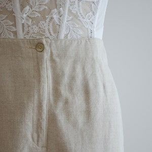 Puede incluir: Pantal&oacute;n de lino beige con cierre de bot&oacute;n y pliegue central. El pantal&oacute;n tiene un corte holgado y una pierna ancha.