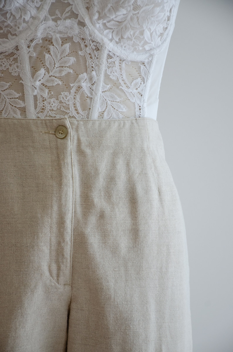 Puede incluir: Pantal&oacute;n de lino beige con cierre de bot&oacute;n y pliegue central. El pantal&oacute;n tiene un corte holgado y una pierna ancha.