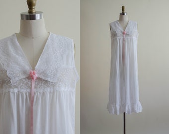 Peut inclure: Une chemise de nuit blanche sans manches avec un décolleté en V, ornée de dentelle et d'un nœud en ruban rose. La chemise de nuit a un ourlet à volants et est présentée sur un mannequin. Un vêtement de nuit d'inspiration vintage.