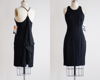 May include: A black sleeveless dress with a draped detail on the back. The dress is on a mannequin and has a tag that says "The Jump".