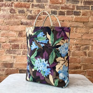 May include: A large tote bag with a floral print featuring blue, green, and brown colors. The bag has two white leather handles.